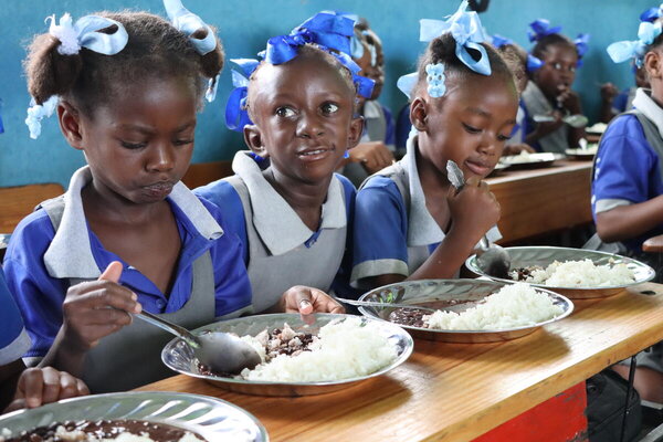Photo: WFP/Alexis Masciarelli. students aged 5 to 7 eat a hot meal in their classroom in the primary school Baptiste Salem in Dondon, where 600 children are registered. Meals are preparing daily with rice and beans food purchased from local producers through WFP Home-Grown School Feeding programme. 