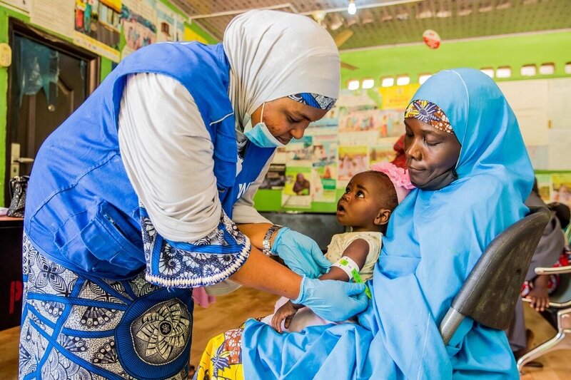 Woman measuring child's upper arm circumference as she sits in her mother's lap