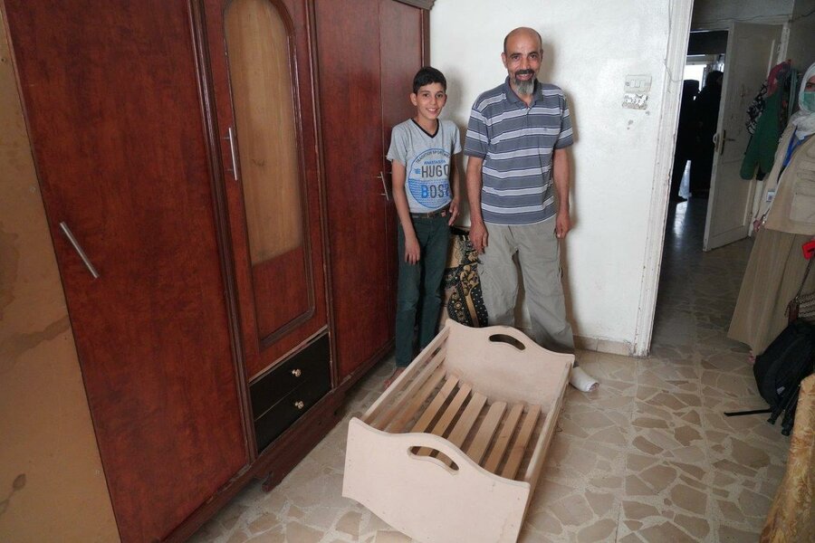 Abo Hashim stands with his older son in front of the crib he made himself for the new baby as he could not afford to buy one.