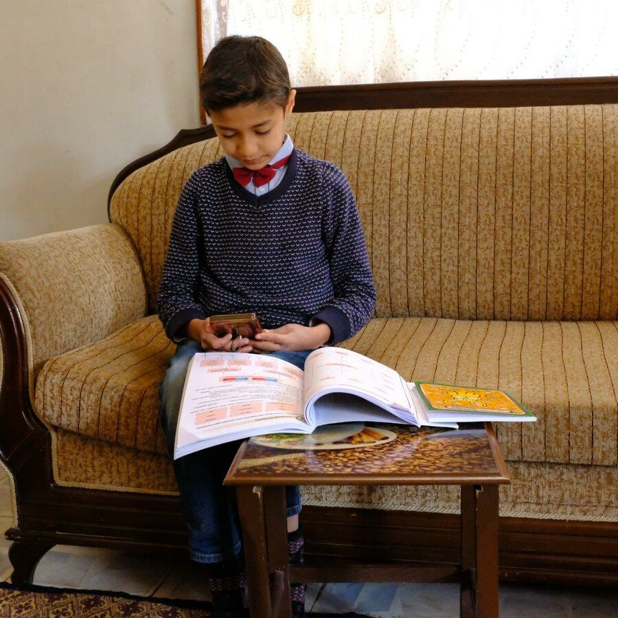 Abdulrafea holds a mobile phone and has a book opened in front of him as he studies remotely during lockdown