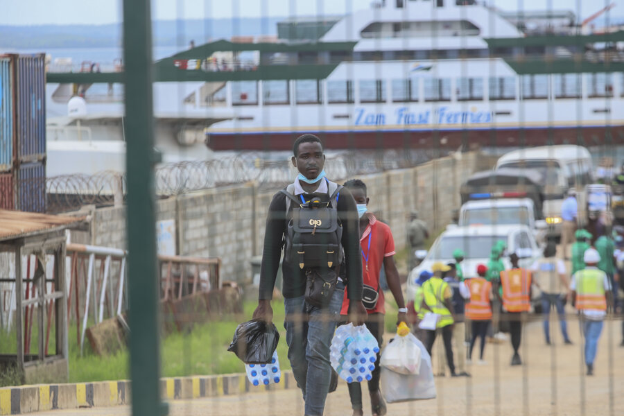 Young man walking off the ferry after escaping attacks in Palma, he is carrying his life possessions in both hands.