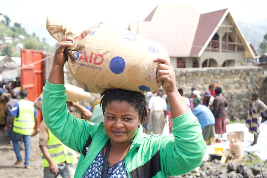 A woman transports a bag of food provisions from USAID by carrying it on her head.