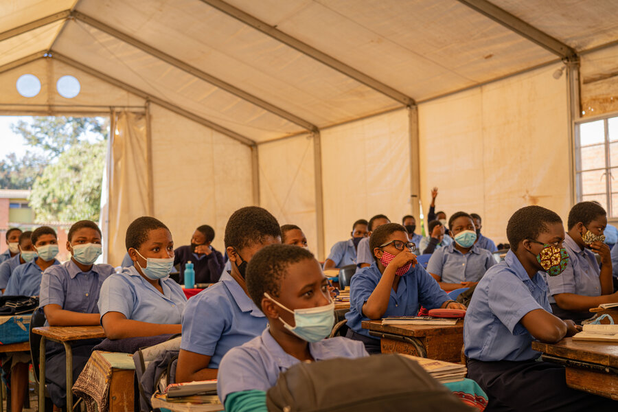 Learners sit in rows at their desks in a spacious tent.