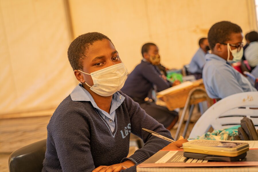 A girl wearing a mask sits at her desk and looks into the camera.