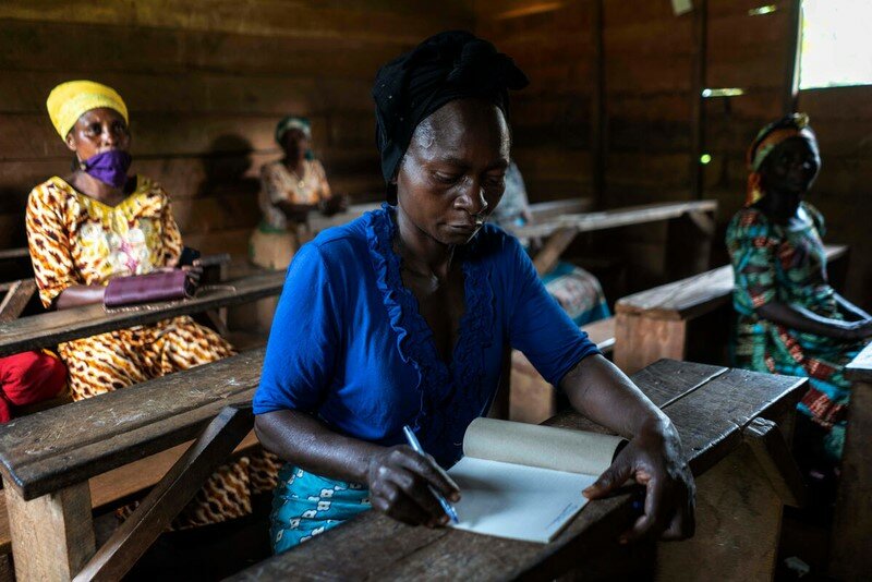 A woman sits at a desk writing in a book.