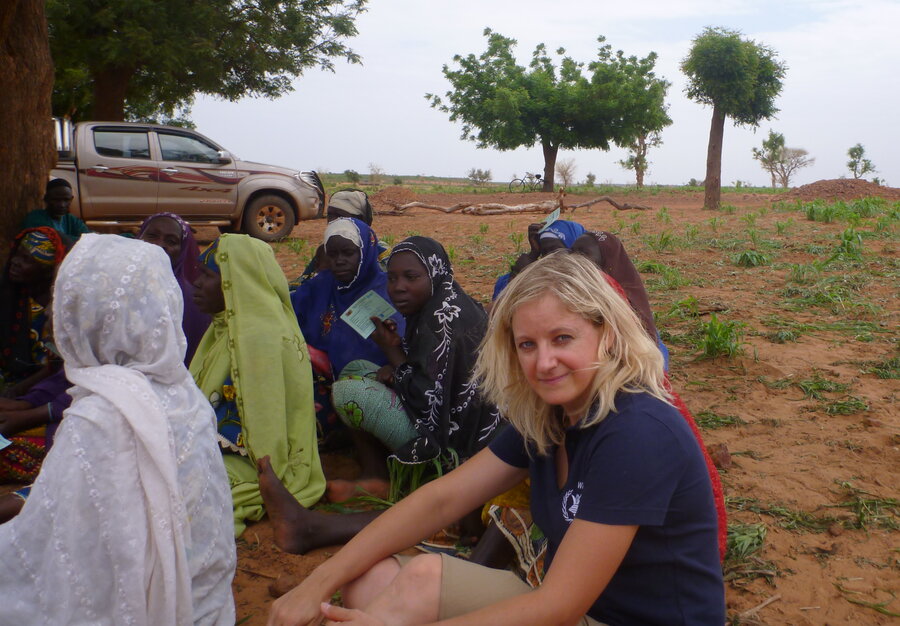 Woman sat outside facing camera side on, with other people in background