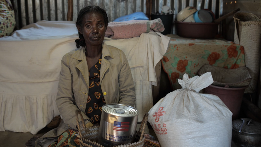 A woman sits with canned food on her lap.