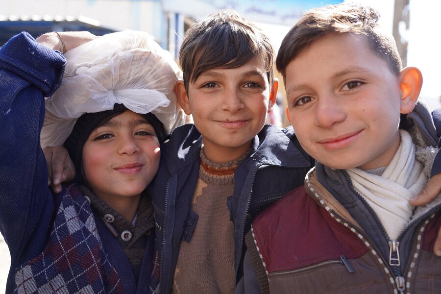 three children and on the left one carries on top of his head a bag of pita bread