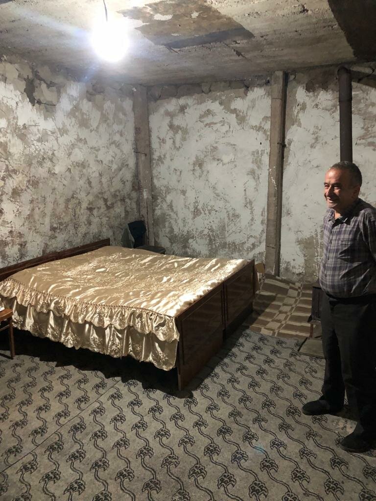 Sahak standing next to his bed in a damp and humid bedroom with mould on the wall and ceiling