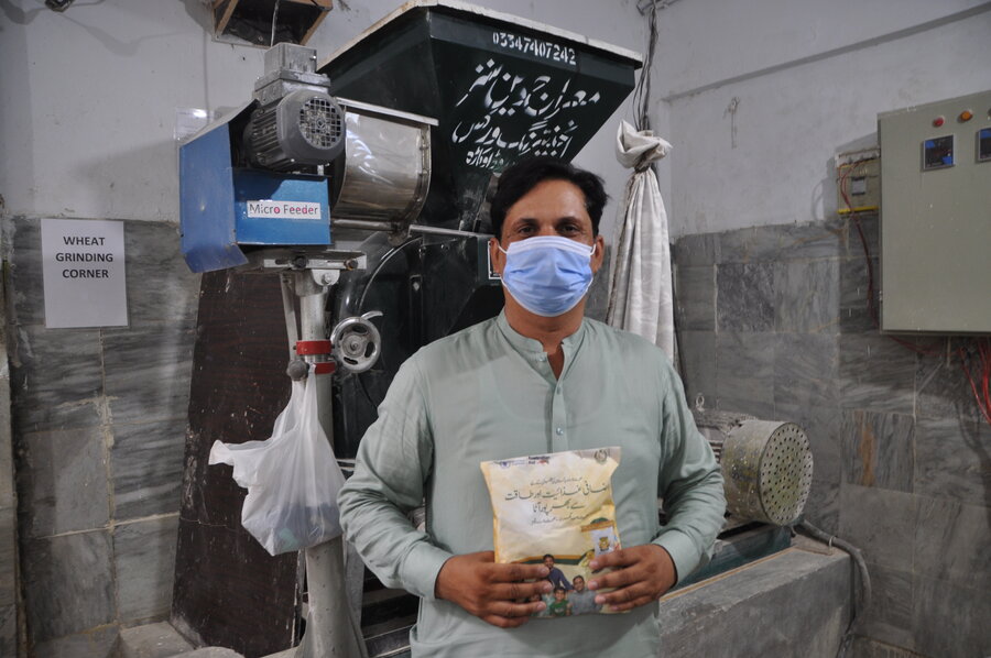 man wearing salwar kameez and face mask, holding packet of flour