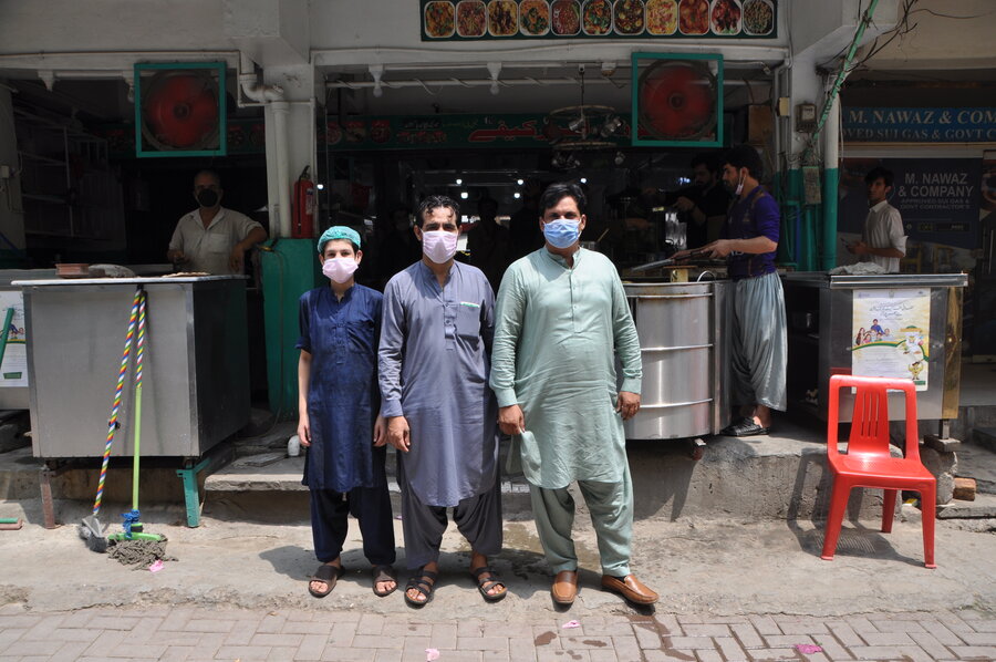 men in salwar kameez and face masks standing in front of shop