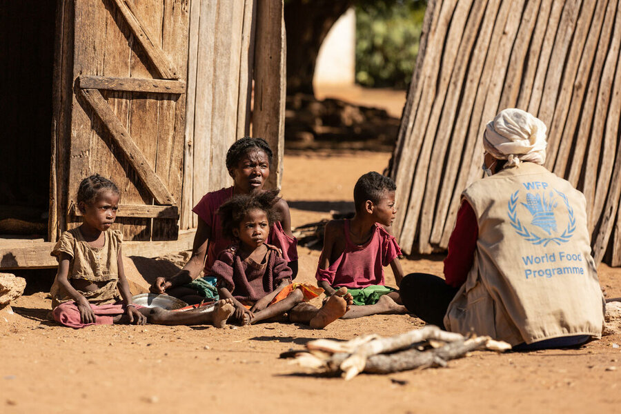 WFP staff member sits on the ground with family outside shelter