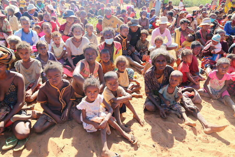 crowd of children and mothers sitting on the ground in the sun