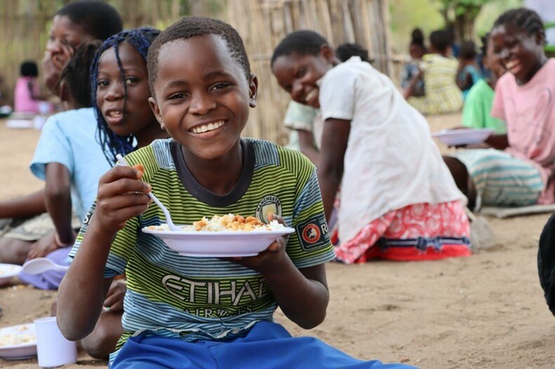 A child smiling while eating food from a white bowl.