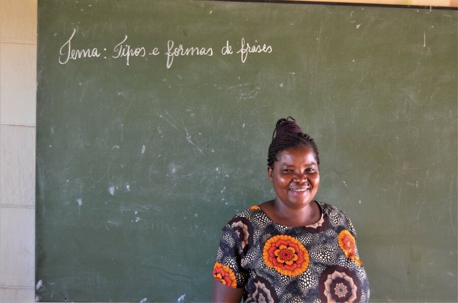 A woman smiling in front of a green chalkboard.
