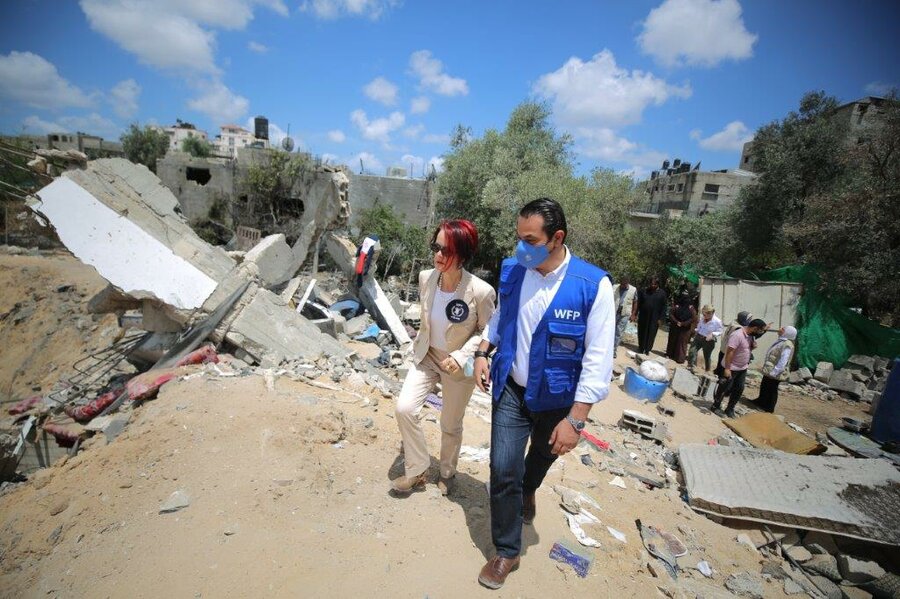 man in blue WFP vest and woman walk through rubble