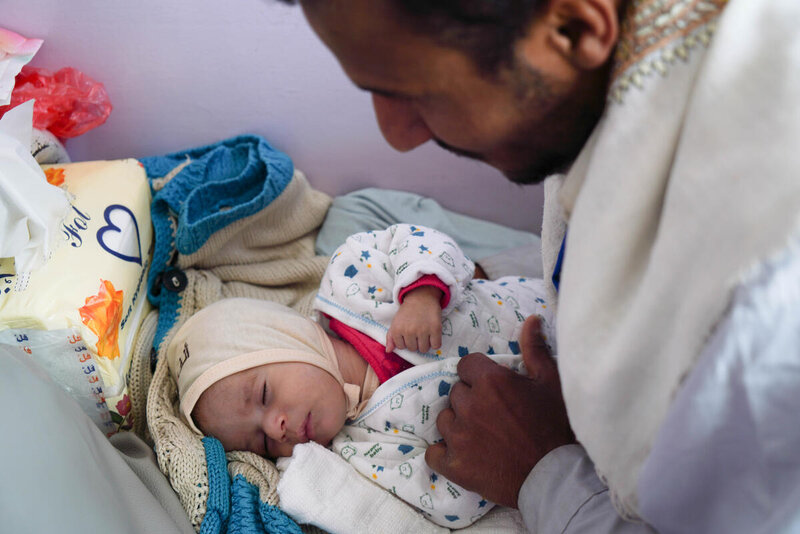 Father Essam leaning over his son who is sleeping on a hospital bed in Al Sabeen Hospital in Sanaa