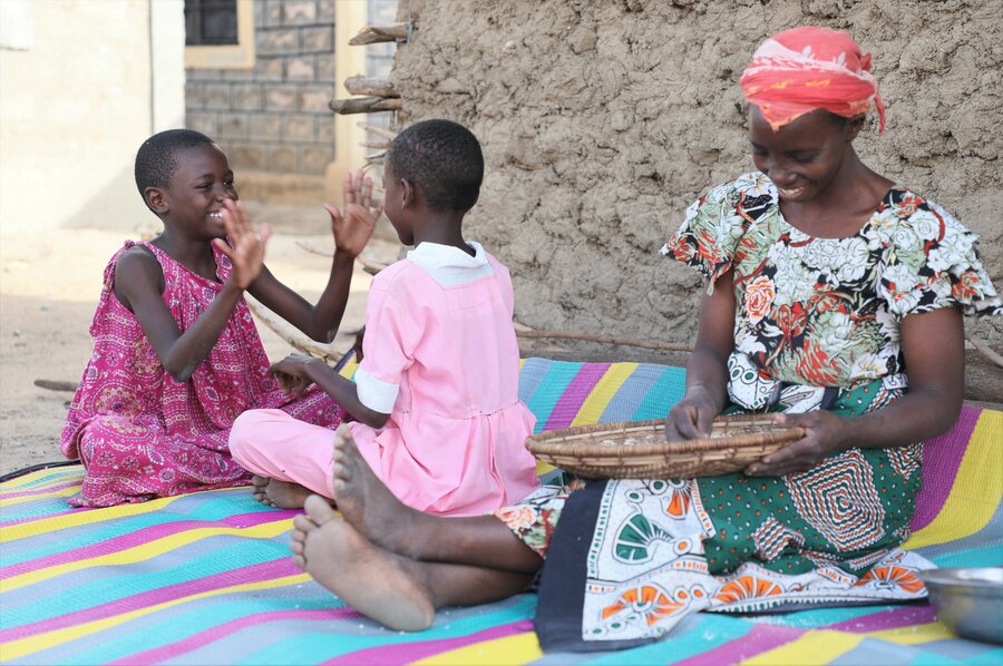 1.	Mwanahamisi sits on a mat outside her hut to prepare a meal for her family as two of her children play together.