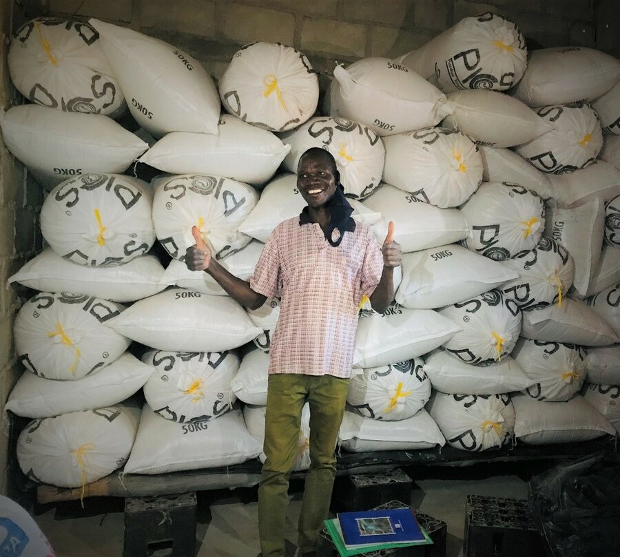 A man stands smiling in front of white bags stacked against a wall.