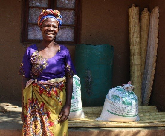 A woman smiles in front of two white bags on her porch.