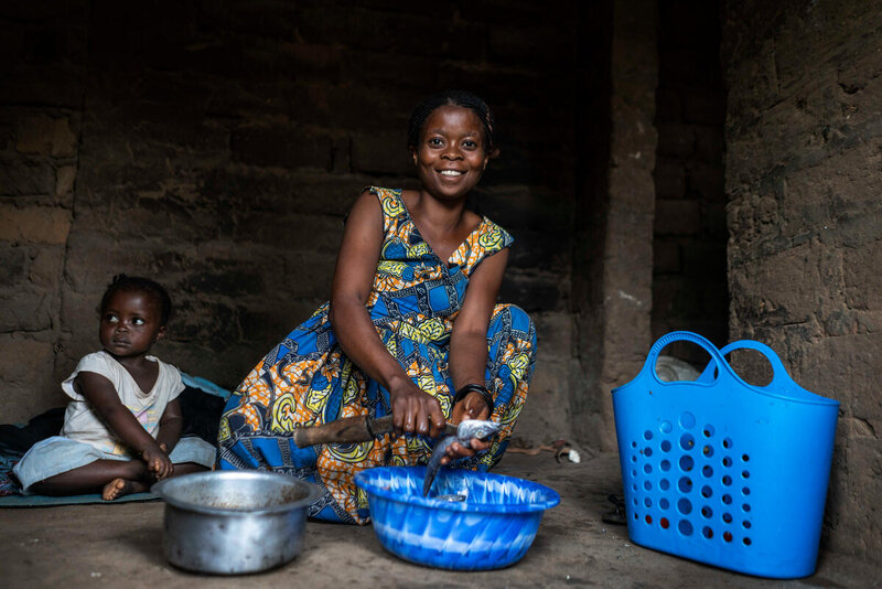 A woman and small girl sit on the floor with a pan and bowl in front of them.