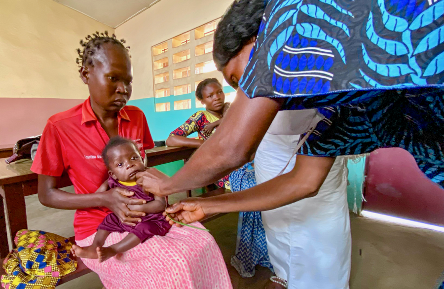 A woman holds a baby while a healthcare worker checks them.
