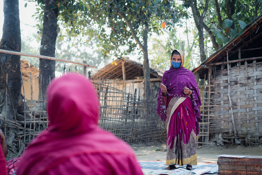 Hason Ara is seen standing up in front of other women who are sitting, she is leading a group discussion