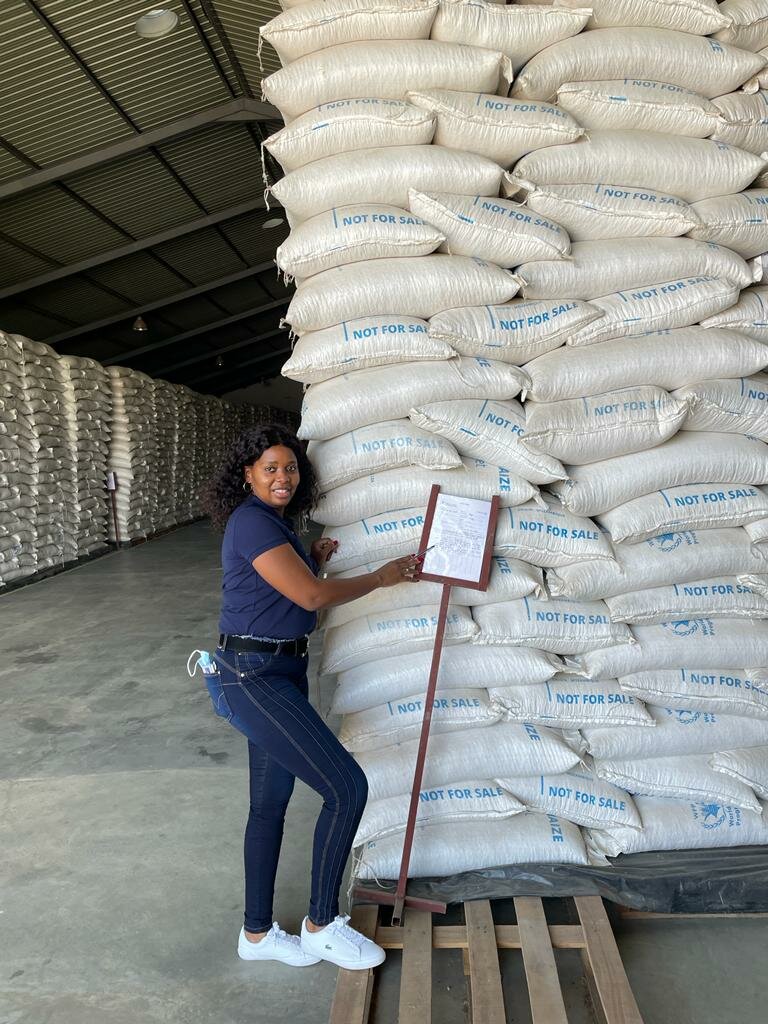 Woman standing next to pile of WFP food in bags, in a warehouse