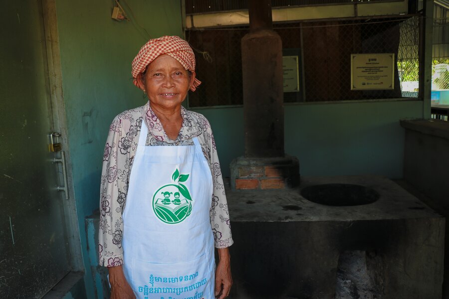 A female Cambodian cook stands in a school kitchen with a smile on her face