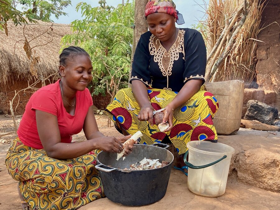 Two women kneel on the ground and prepare food