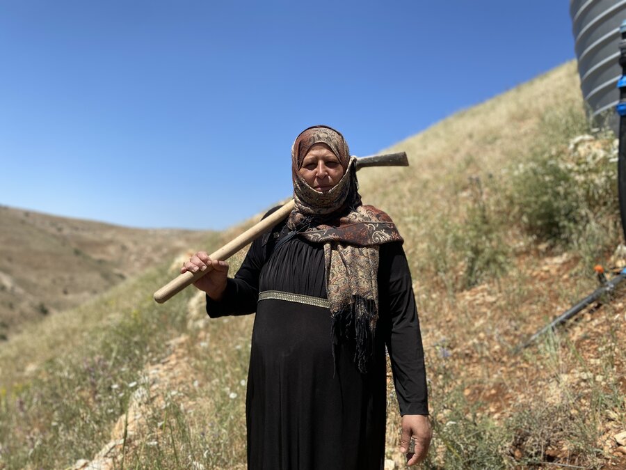 A female farmer in a field holds a farming tool over her shoulder