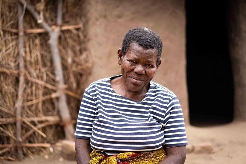 A woman in a black and white striped shirt stands in front of her home