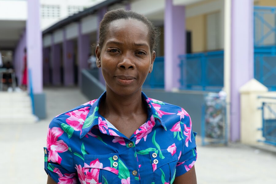 A female wearing a blue and pink flowered shirt stands in a school yard