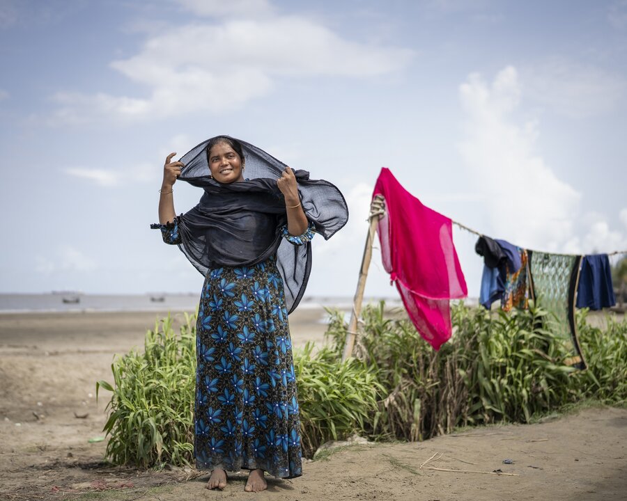 A woman adjusts her sari while standing in a field in front of her washing line