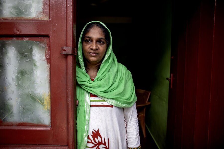 A woman wearing a green headscarf looks out of a red doorway