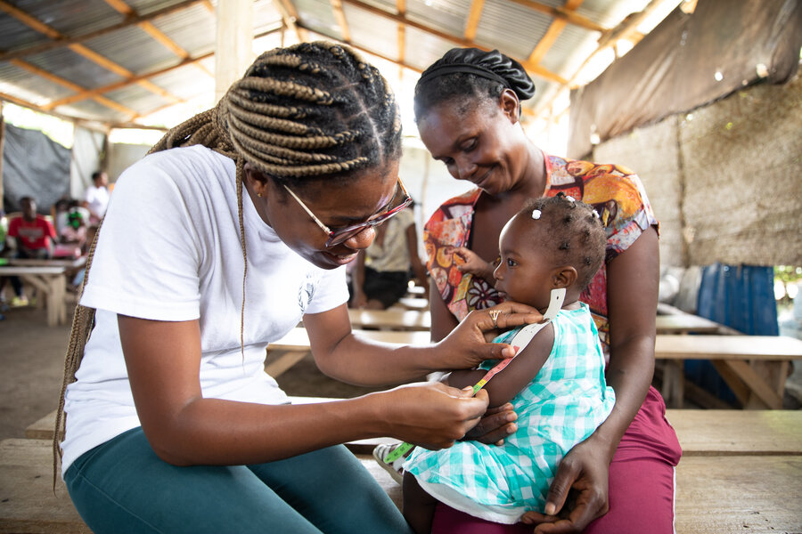 A mother holds her daughter whose arm is being measured to check for malnutrition