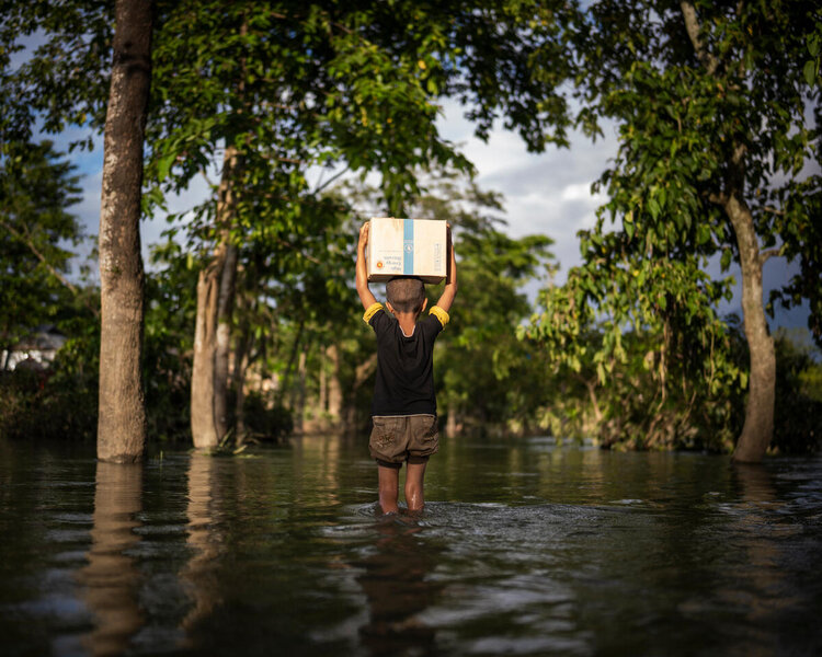 a child is carrying a box over his head while he is walking in a flooded area