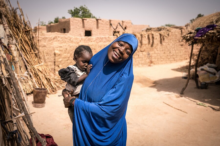 A mother holding a baby in Niger with her village in the background