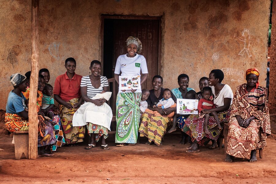 A group of women sit in a line next to their teacher at a nutrition training