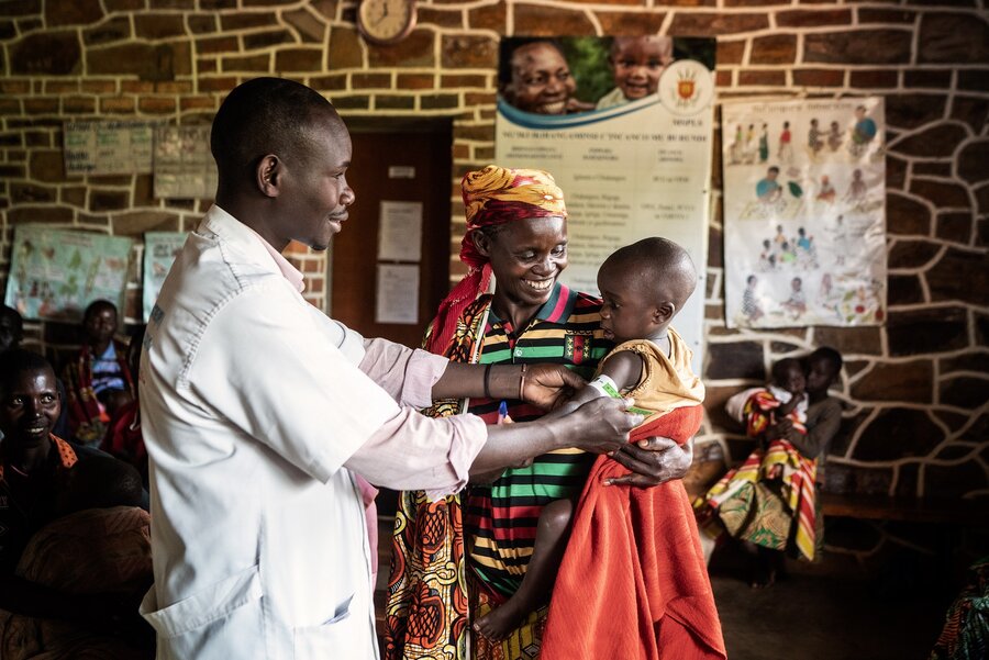 A medical professional checks a baby for malnutrition while they are held by their mother in a clinic