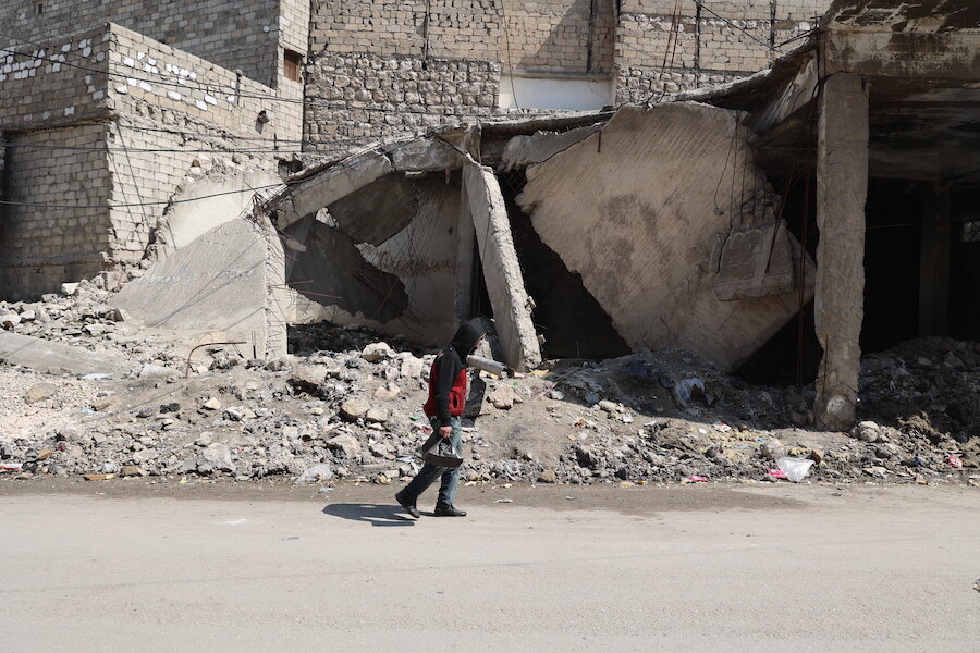 Person walking past a ruined building