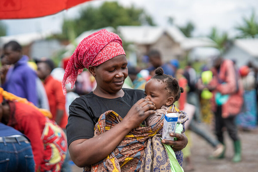 A mother in a read headwrap holds her baby daughter in an IDP camp in DRC