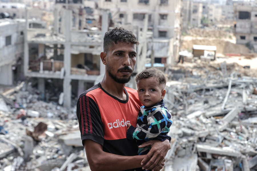 Man holding child in front of ruined buildings
