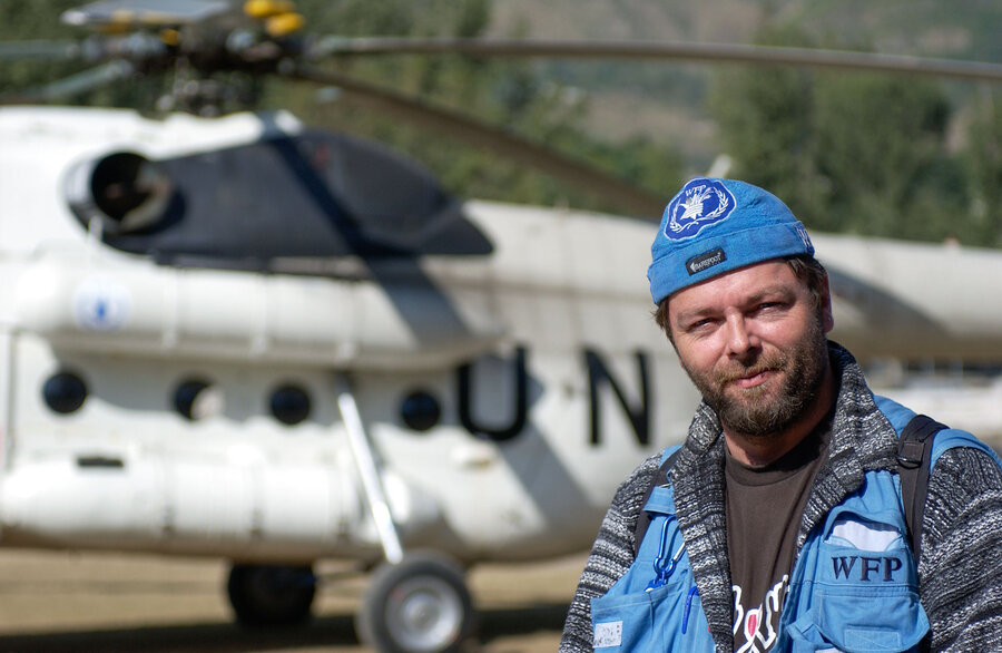 A man wearing a blue WFP-logo hat and vest in front of a UN helicopter