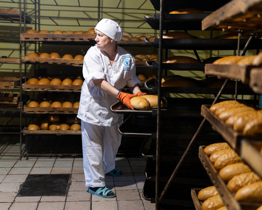 A female baker looks to her right handling a tray of bread in a cooling room