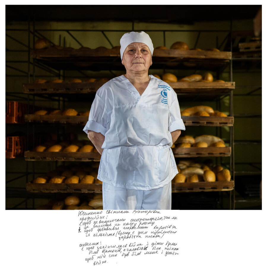 A woman in a white baker's outift with a WFP logo stands in front of rows of freshly baked bread