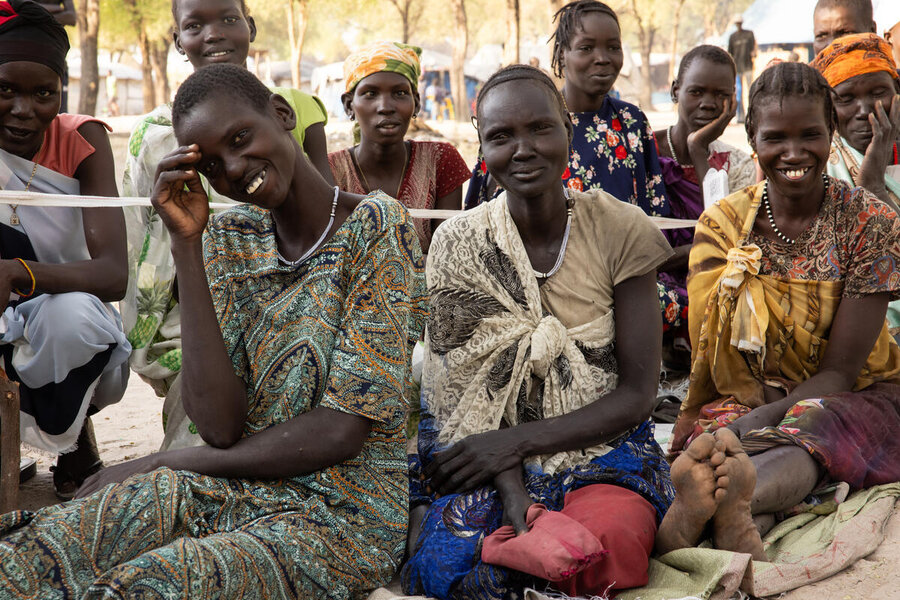 Three women sat on the ground at an outdoor registration in South Sudan smile 