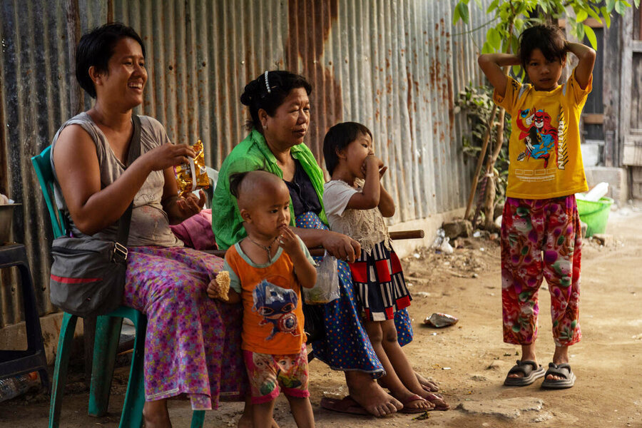Two women sit in an outdoor area surrounded by children