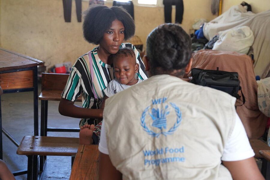 A woman in stripey dress holds her daughter on her lap as the talks to a WFP staff who has her back to the camera