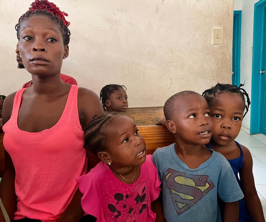 A woman in a pink vest waits in line with three children next to her
